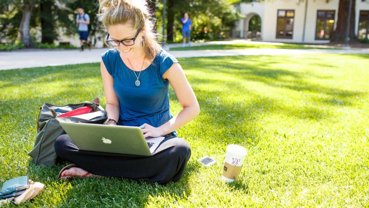 A student sitting on the lawn studying with her laptop 