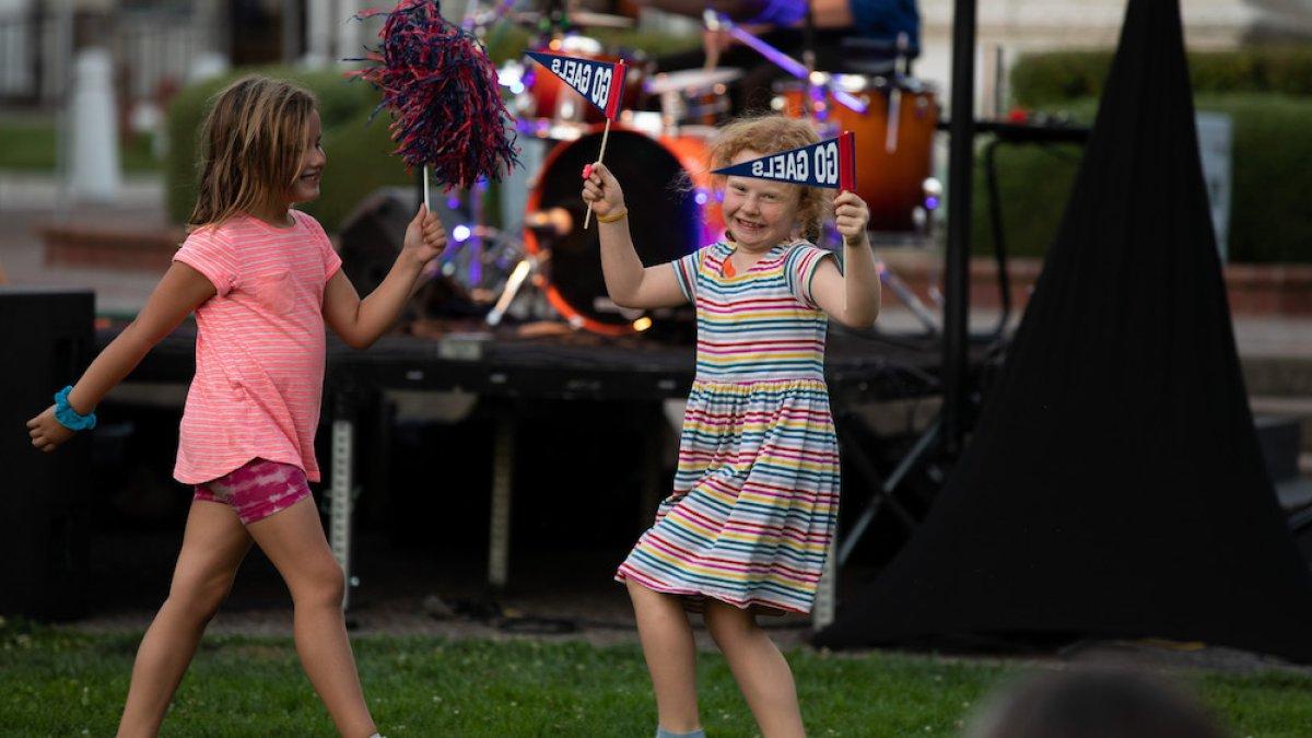 Two school-aged girls wave pom poms and pennants