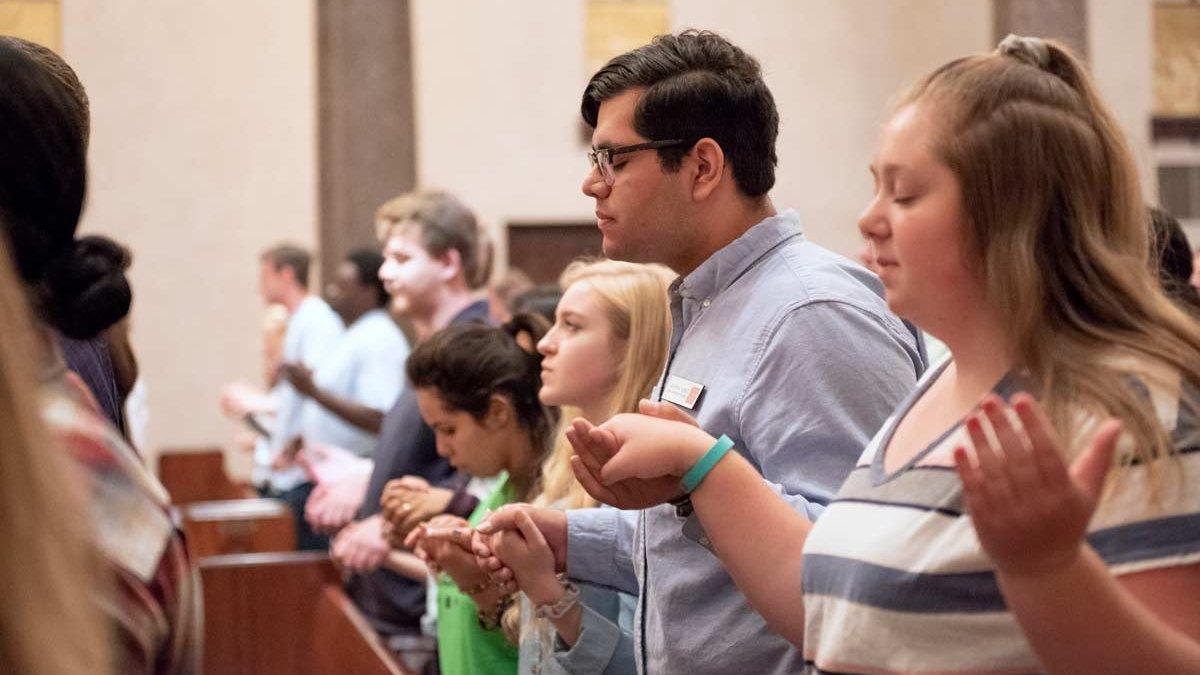 Students holding hands praying during mass